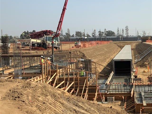 Workers pouring concrete for one of the facility's footings next to a pedestrian corridor (l)